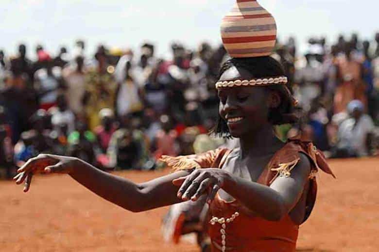 Traditional Ugandan dancer balances a clay pot on her head during a vibrant cultural celebration — experience Uganda with GoFurther 4x4 Car Rental.