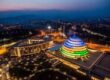 Aerial night view of the Kigali Convention Centre in Rwanda, illuminated in vibrant blue, yellow, and green lights, symbolizing the national flag colors.
